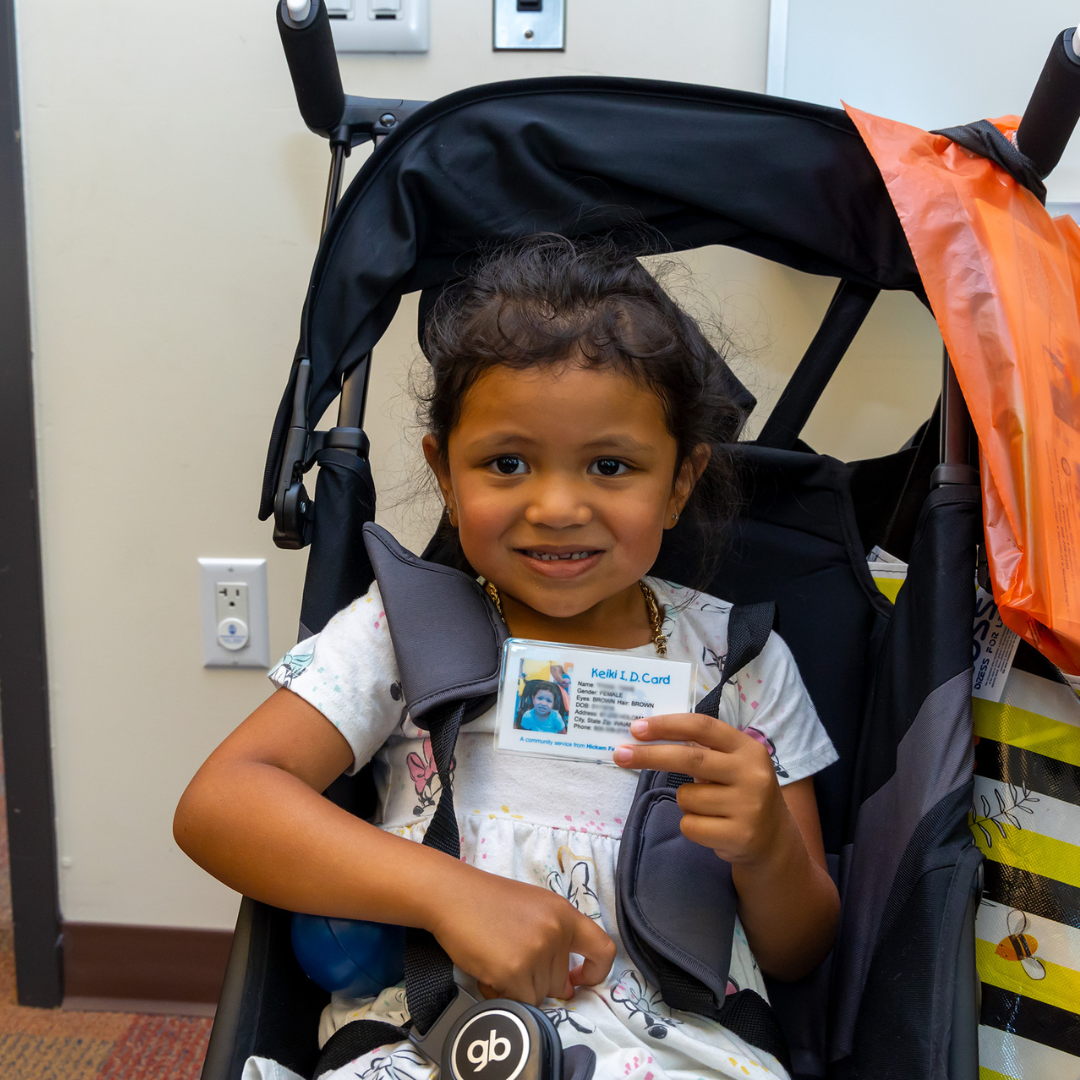 A little girl holding an ID up while sitting in a stroller