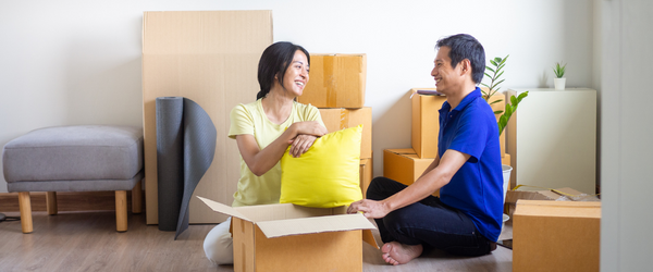 A couple sitting on the floor amidst boxes and furniture